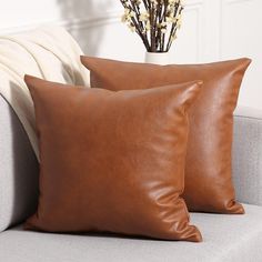 two brown leather pillows sitting on top of a couch next to a vase with flowers