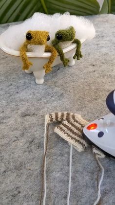 two stuffed frogs are sitting in a bathtub on a table next to an ironing board