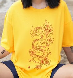 Be a trend-setter in our River Dragon Tee! Flaunt your bad-ass attitude with the cool dragon print, while still maintaining comfort with the 100% cotton, relaxed fit. You're no princess, you're a dragon ready to take on the streets. 🐉 Ain't no one gonna stop you! This is a unisex tee so check the size guide for measurements! and if you want to rock that oversized look go up a few sizes. This product is made especially for you as soon as you place an order, which is why it takes us a bit longer Cotton T-shirt With Dragon Print, Short Sleeve Tops With Dragon Print For Streetwear, Dragon Print Crew Neck Top For Streetwear, Casual Crew Neck T-shirt With Dragon Print, Casual Dragon Design Tops For Streetwear, Streetwear Short Sleeve T-shirt With Dragon Print, Cotton T-shirt With Dragon Print Short Sleeve, Dragon Print Cotton T-shirt For Streetwear, Streetwear Dragon Print Short Sleeve T-shirt