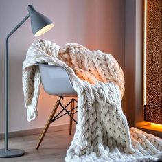 a white blanket sitting on top of a chair next to a lamp and a wall