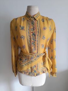 Vintage 80's semi sheer yellow silk shirt, blouse, with a floral print in shades of teal and pink.   A matching silk triangle that can be used as a scarf or a belt makes the set. Ovesized shoulders with small, soft shoulder pads and long sleeves with cuffs. Button up front with small golden lucite buttons. No tags, but it dresses a size M/L, depending on the desired fit. Please check measurements for accuracy: Shoulders: 40cm/15.8" Bust: 102cm/40.1" Length: 58cm/22.8" Sleeve: 59cm/23.2" In very Yellow Floral Print Silk Tops, Yellow Silk Top With Floral Print, Yellow Floral Print Silk Blouse, Yellow Silk Blouse With Floral Print, Vintage Fashion Long Sleeve Summer Blouse, Vintage Fashion Summer Long Sleeve Blouse, Summer Vintage Fashion Long Sleeve Blouse, Long Sleeve Blouse For Vintage Summer Fashion, Yellow Bohemian Blouse For Daywear