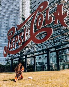 a woman sitting on the ground in front of a building with a large coca cola sign