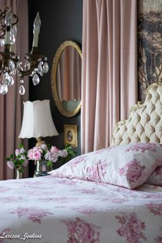 a bed with pink and white flowers on it in front of a chandelier