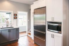 an empty kitchen with stainless steel appliances and wood flooring, along with white cabinets