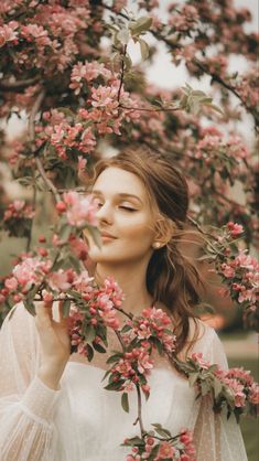 a woman standing under a tree with pink flowers