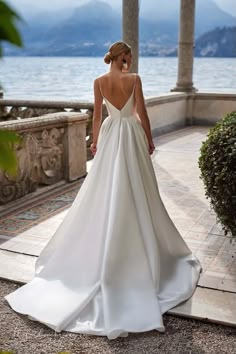 a woman in a white wedding dress is standing by the water with her back to the camera