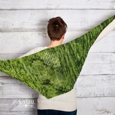 a woman holding up a green shawl in front of a white wooden wall,