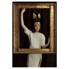 a woman in a white dress is holding up a gold frame with two golden crowns on her head