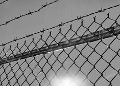 black and white photograph of a fence with the sun shining through it's barbed wire