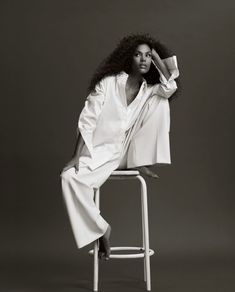 a woman sitting on top of a white chair wearing a white shirt and long pants