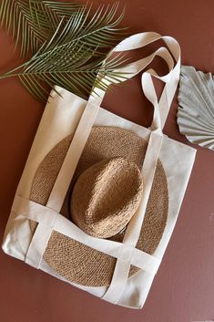 a straw hat sits on top of a tote bag next to a palm leaf