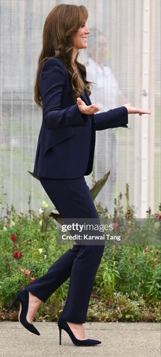 a woman in a suit and heels walking on the sidewalk with her hand out to someone