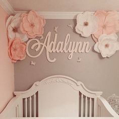 a baby's room decorated with pink and white flowers on the wall, along with a name sign