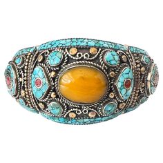 This vintage Tibetan bracelet is a bold and vibrant piece of jewelry that captures the essence of Himalayan craftsmanship. The bracelet is chunky and substantial, designed to make a statement with its striking combination of materials and colors. The bracelet is primarily crafted from silver, with a solid, robust structure that gives it a weighty feel. Throughout the surface, silver and brass alternate, creating a dynamic interplay of metals that adds texture and depth to the piece. The brass se Swirling Clouds, Tibetan Bracelet, Earthy Aesthetic, Tibetan Jewelry, Chunky Bracelet, Tibetan Turquoise, Turquoise Bracelet Cuff, Chunky Bracelets, Cool Tones