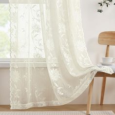 a white curtain hanging in front of a window next to a chair and potted plant