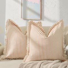 two pillows sitting on top of a couch in front of a framed painting and lamp