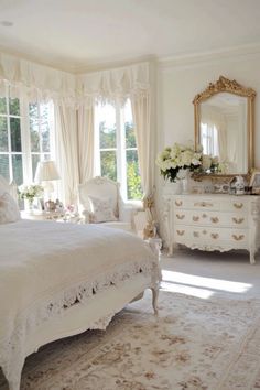 a white bed sitting in a bedroom next to a dresser and window covered with curtains