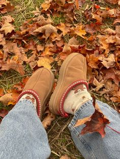 someone wearing slippers and jeans standing in the leaves