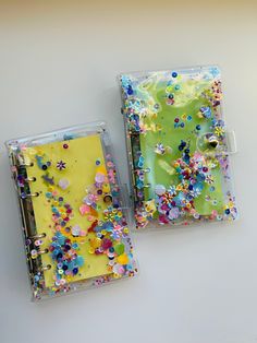 two small notebooks covered in colorful confetti and plastic wrappers on a white surface