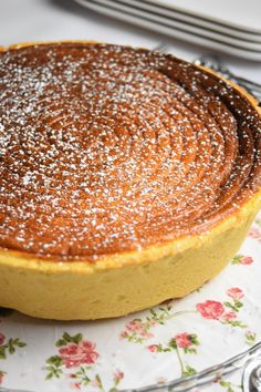 a cake on a plate covered in powdered sugar sits on a floral tablecloth