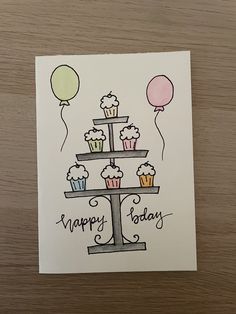 a happy birthday card with cupcakes and balloons on the top, in front of a wooden table