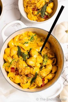 two bowls filled with pasta and vegetables on top of a white tablecloth next to pumpkins