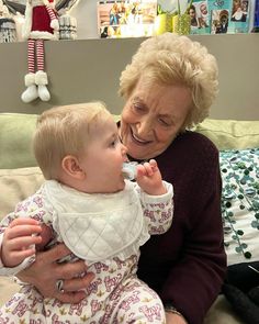 an older woman is brushing her teeth while holding a baby in her lap and smiling at the camera