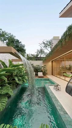 an outdoor swimming pool surrounded by plants and greenery with a waterfall running down the side