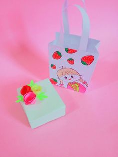 a paper bag with strawberries on it next to a small gift bag that is shaped like a strawberry