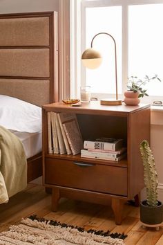 a nightstand with books on it next to a bed and a window in the background