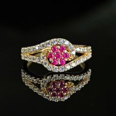 a gold ring with pink and white stones on it's side, sitting on a black surface