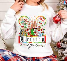 a woman wearing mickey mouse birthday shirt next to a christmas tree with ornaments on it