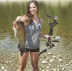 a woman holding a fish while standing next to a bow and fishing pole in the water