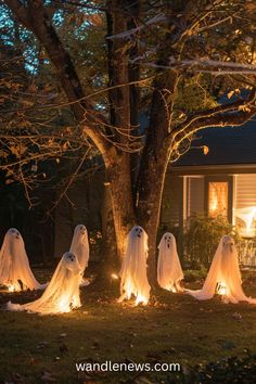 halloween decorations in front of a house with ghost figures on the lawn and trees lit up at night