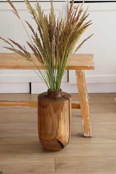 there is a vase with some plants in it on the floor next to a bench