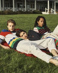 three young people laying on the grass in front of a large house and one is holding a frisbee