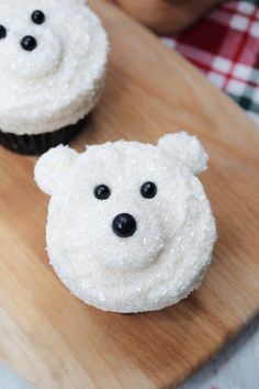 two cupcakes with white frosting and black eyes are on a cutting board