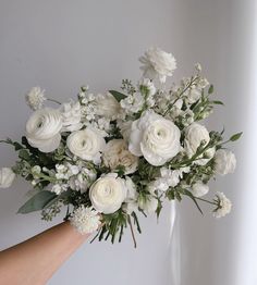 a bouquet of white flowers being held by someone's hand in front of a wall