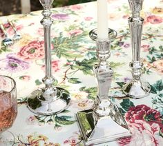 two silver candlesticks sitting on top of a table next to a wine glass