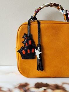 an orange purse with black and red decorations hanging from it's handle, sitting on a table