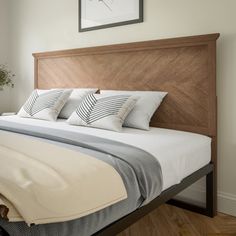 a bed with white sheets and pillows in a bedroom next to a potted plant