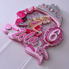 a pink and silver sign with barbie dolls on it's side, surrounded by other decorations