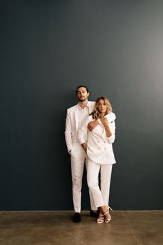 a man and woman standing next to each other in front of a blue wall wearing white