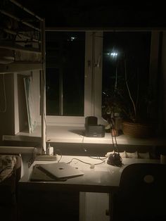 a dark room with a desk, computer monitor and lamp in the window sill