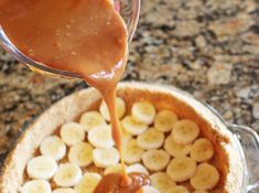 a person pouring caramel sauce over bananas in a pie pan on a granite counter