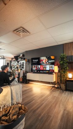 a man sitting on a couch watching tv in a living room with wood floors and walls