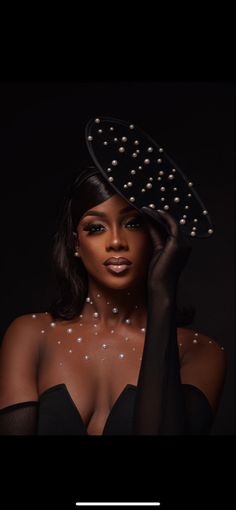 a woman in black with pearls on her head and hands behind her head, wearing a hat