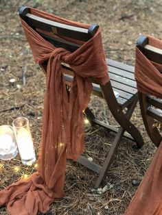 two wooden chairs sitting on top of a field covered in grass next to a lit candle