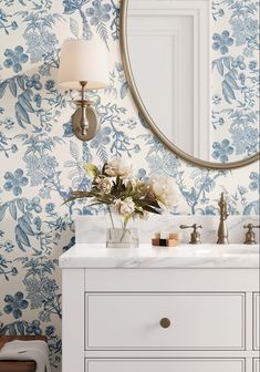 a bathroom vanity with blue cabinets and a round mirror above it, next to a white flower arrangement