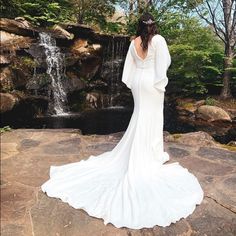 a woman in a white wedding dress standing on rocks near a waterfall with her back to the camera